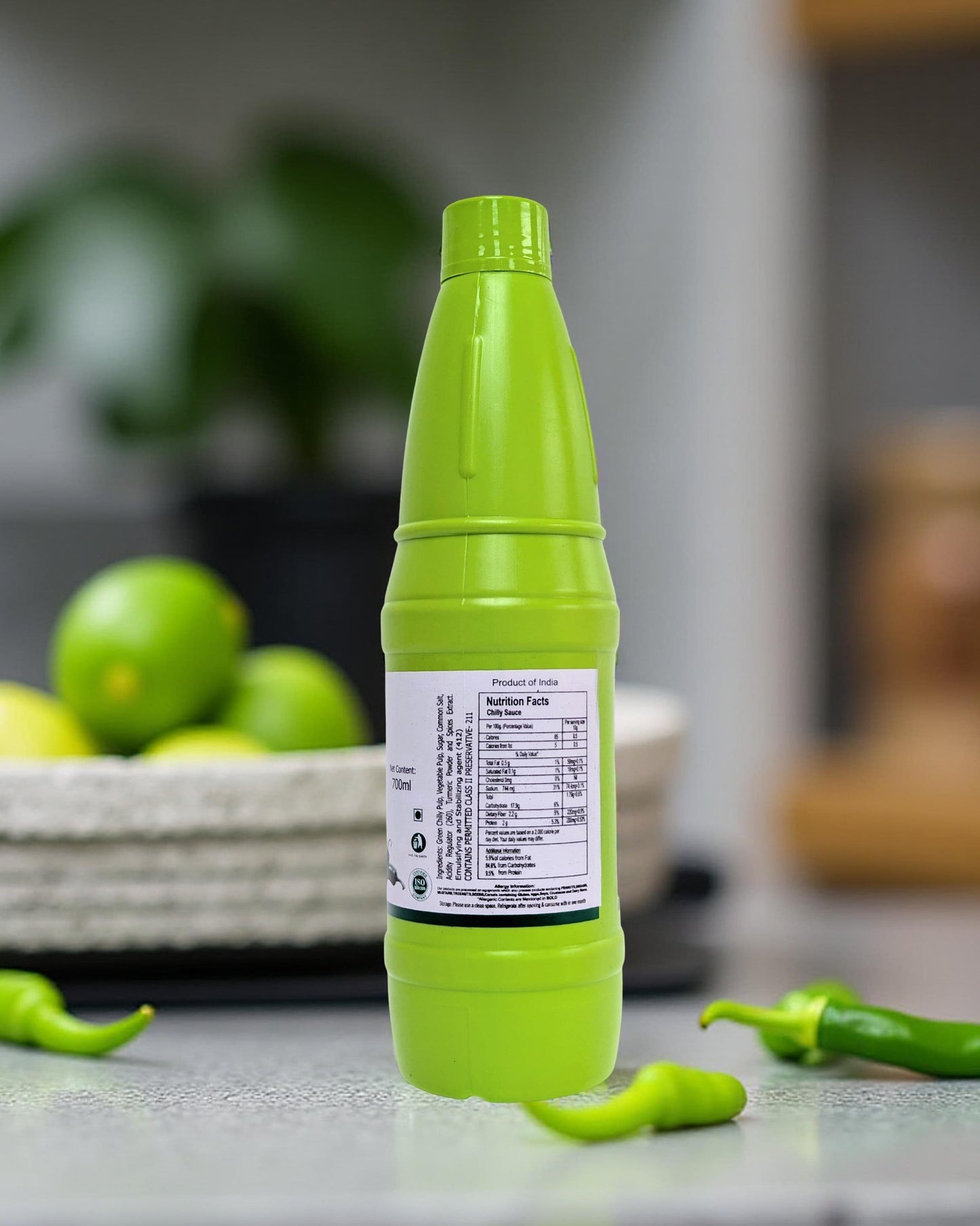 Green bottle with a label on a kitchen counter with limes and peppers in the background