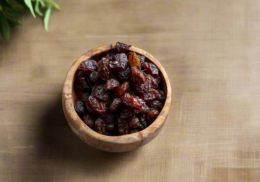 Wooden bowl filled with raisins on a wooden surface