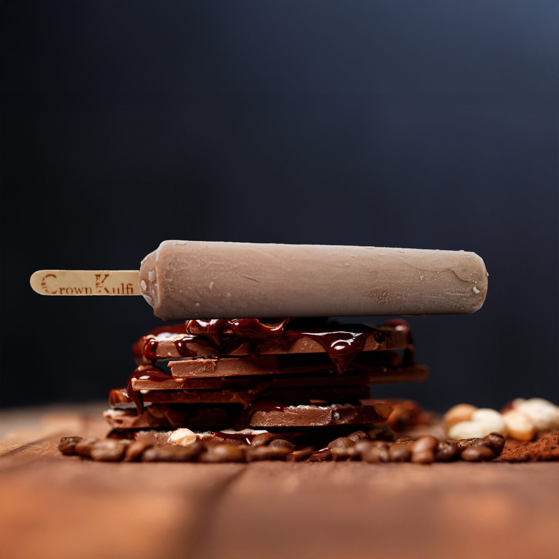 Chocolate popsicle with a rolling pin on top of chocolate pieces and coffee beans against a dark background