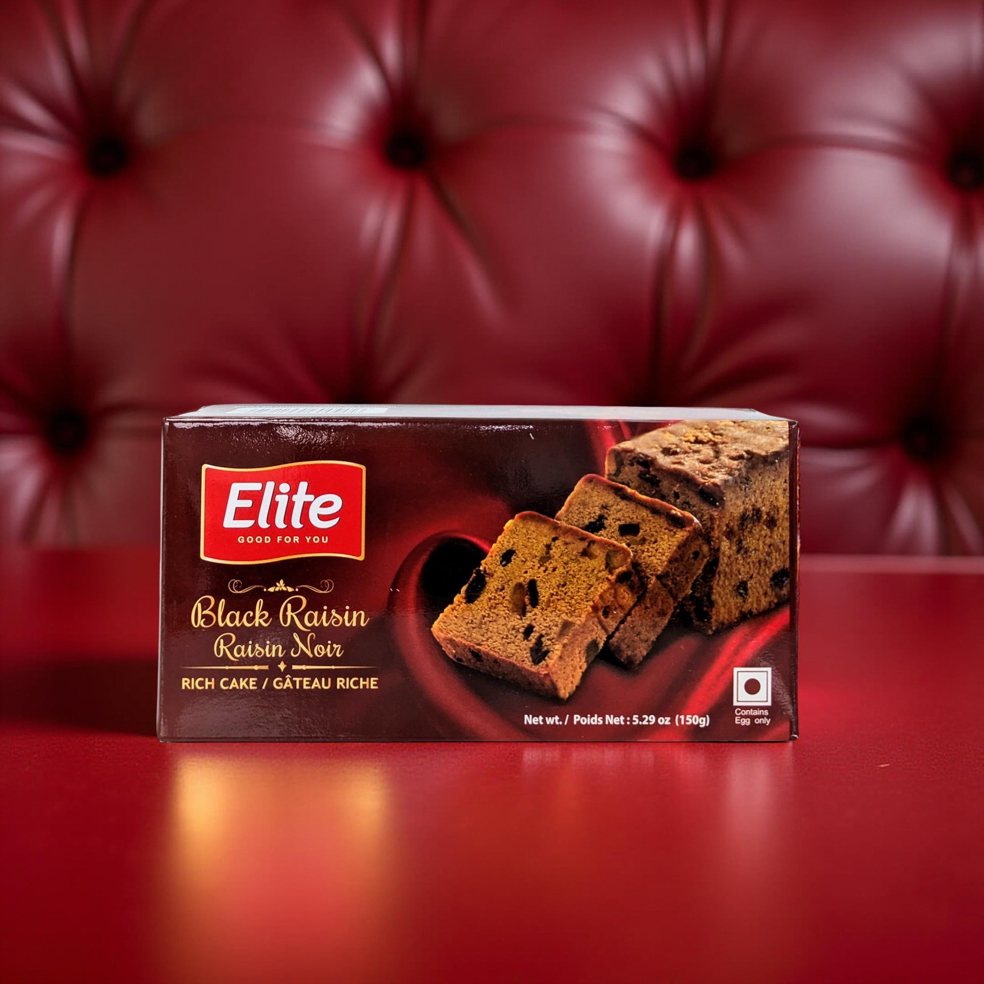 Box of Elite Black Raisin Rich Cake on a red surface with a red textured background