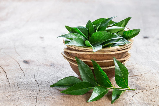 Green curry leaves in a woven basket on a wooden surface