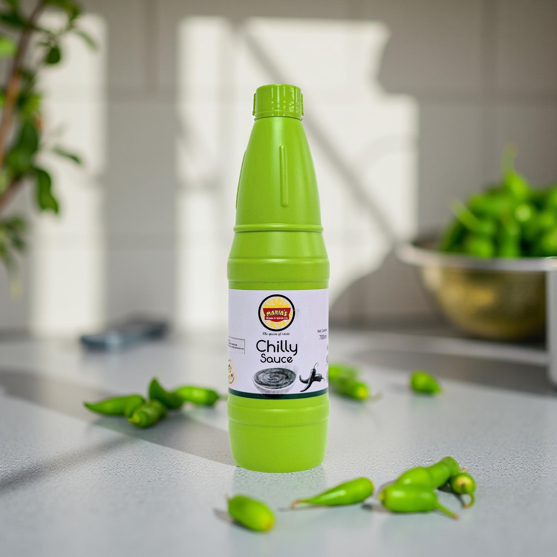 Green bottle of Chilly Sauce on a kitchen counter with green peppers.