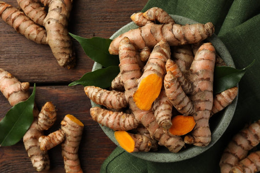 Turmeric roots in a bowl with leaves on a wooden surface