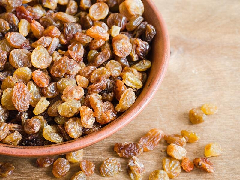 Dried raisins in a terracotta bowl on a wooden surface